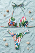 Colorful tropical print bikini set on a gray surface with decorative elements.