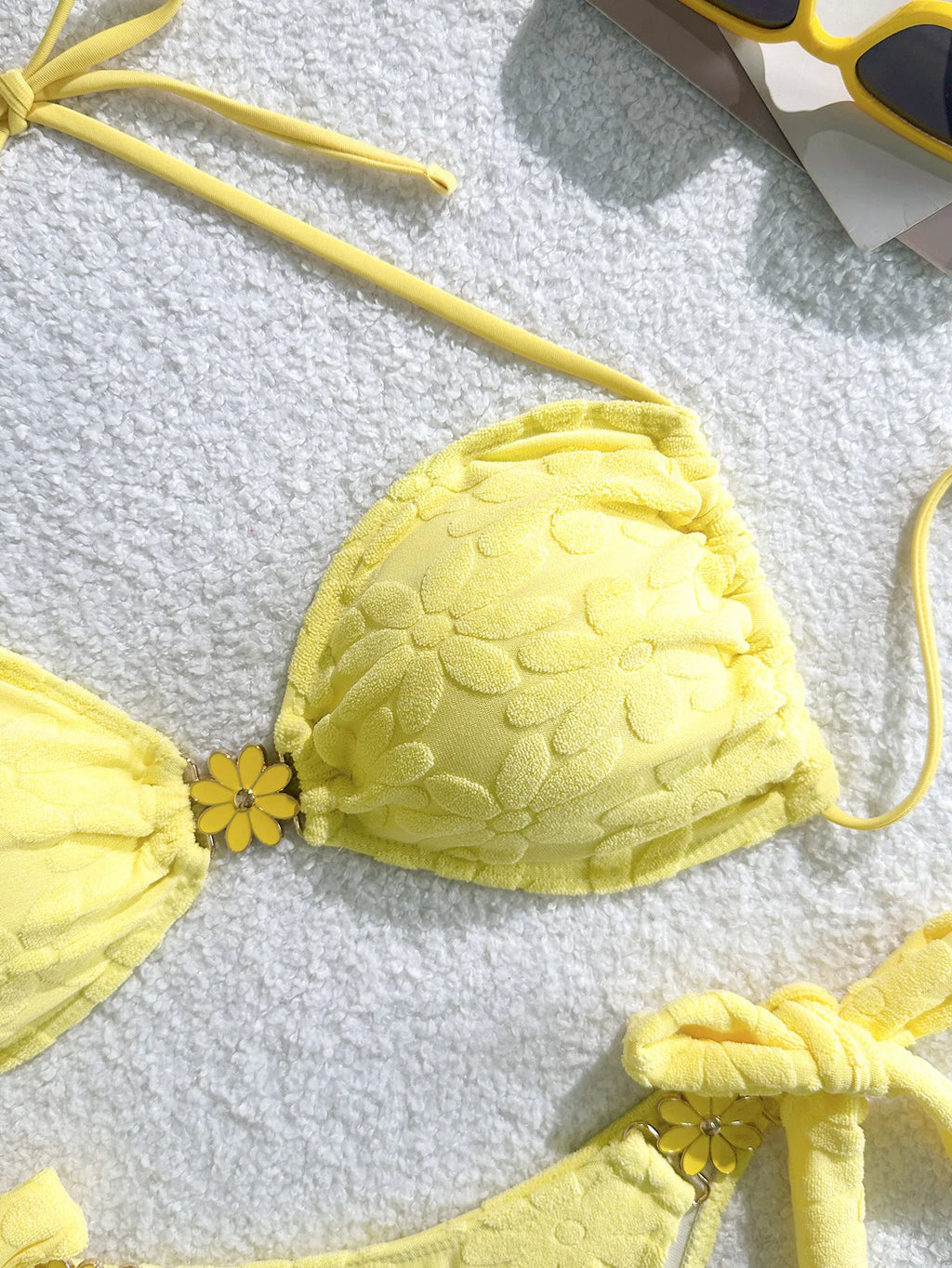 Yellow bikini top with floral details on a textured surface